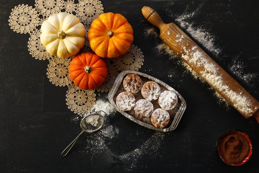 Flat lay of pumpkins, pastries, rolling pin, and sieve on a dark surface.