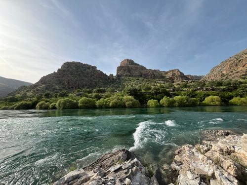 Free Breathtaking view of mountains and a clear river with lush greenery under a blue sky. Stock Photo