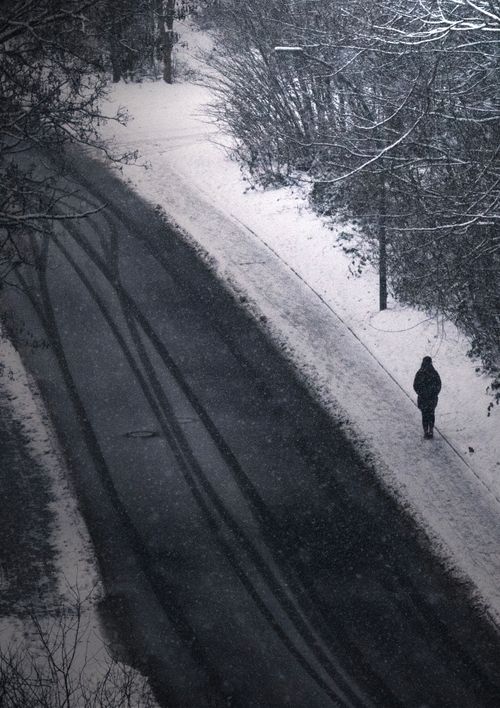 Free A solitary figure walks along a snow-covered road in Flintbek, Germany, depicting serene solitude. Stock Photo