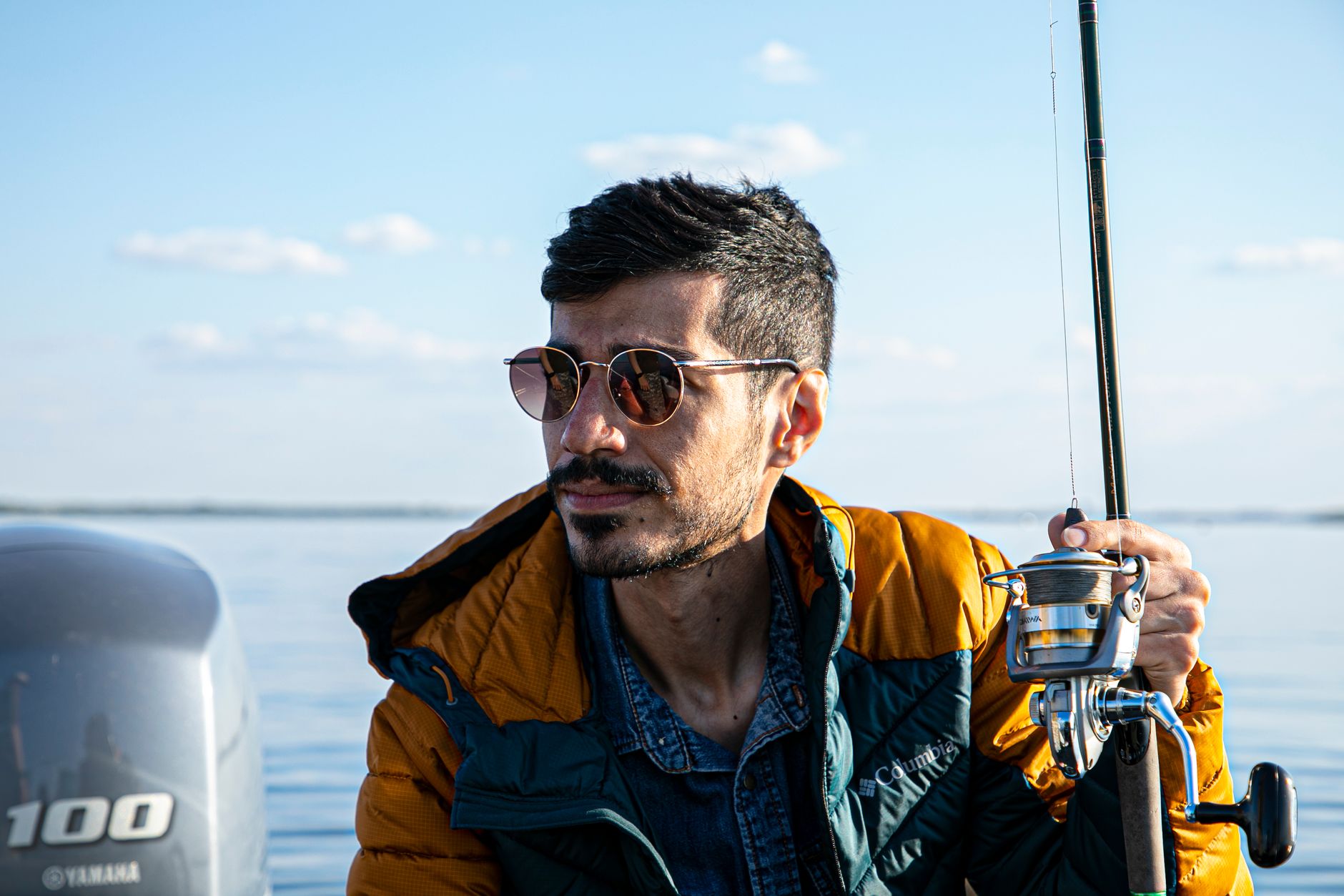 A man wearing sunglasses enjoys fishing on a calm sea during a sunny day.