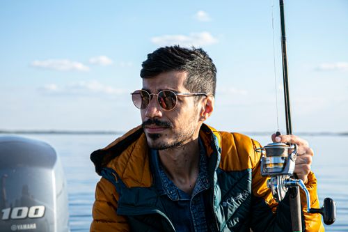 Free A man wearing sunglasses enjoys fishing on a calm sea during a sunny day. Stock Photo
