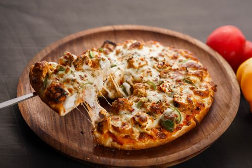 Free Appetizing close-up of a cheesy vegetable pizza on a wooden plate with a slice being served. Stock Photo