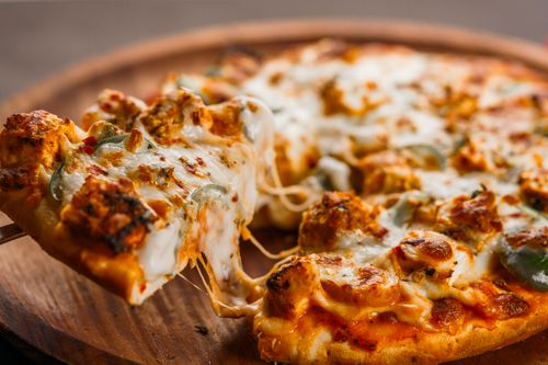Free Close-up of a hot cheesy pizza being served with flavorful toppings on a wooden platter. Stock Photo