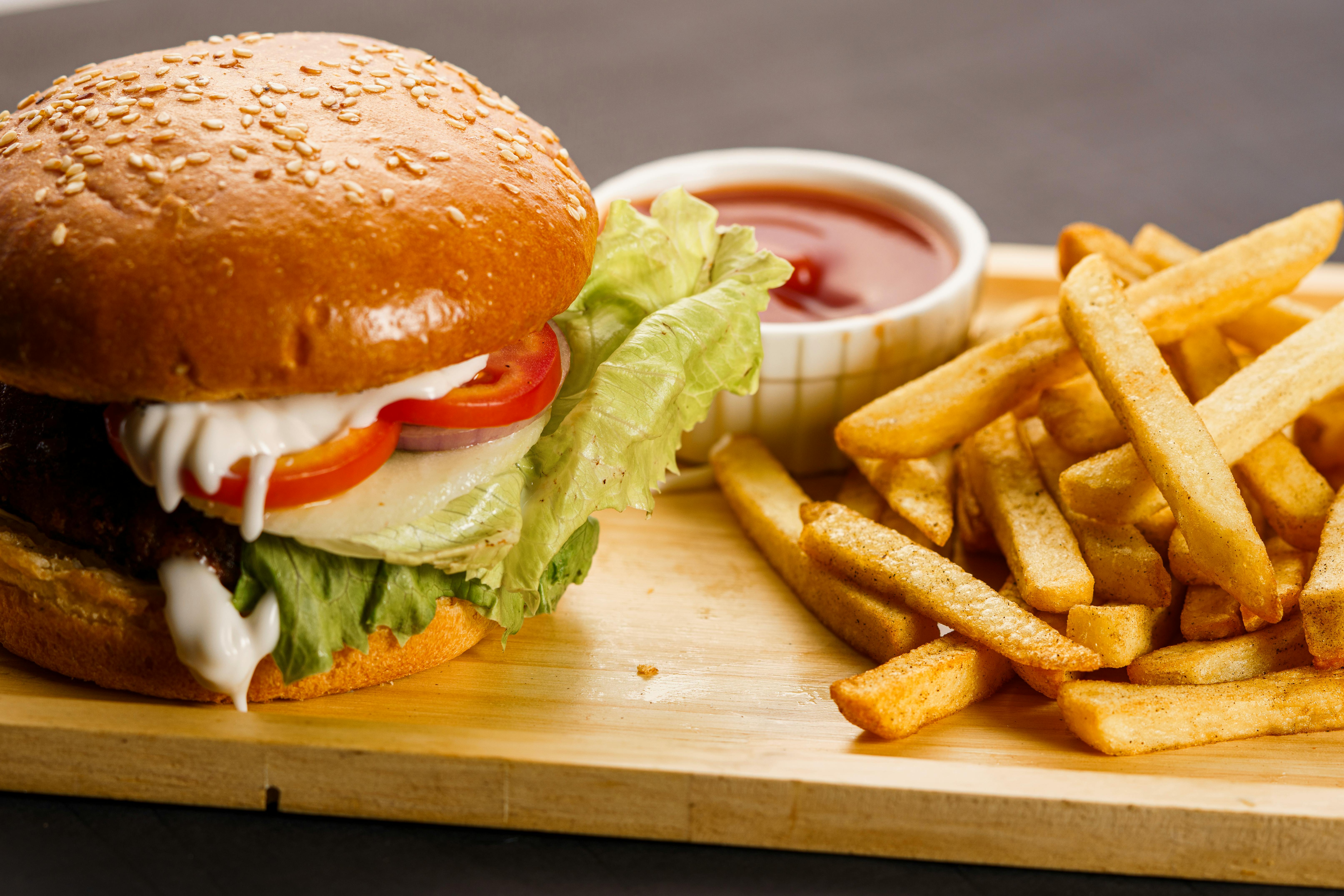 免費 一個多汁的起司漢堡的特寫鏡頭，上面有新鮮的薯條和番茄醬在木盛肉盤上。 圖庫相片