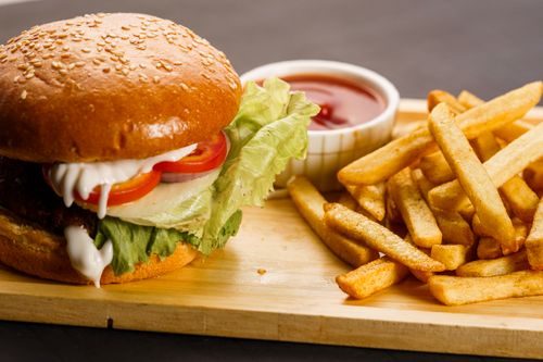 Free Close-up of a juicy cheeseburger with fresh fries and ketchup on a wooden platter. Stock Photo