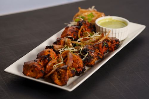 Free A flavorful chicken tikka dish served with a side of green chutney and garnishes on a white platter. Stock Photo