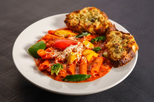 Free Tasty penne pasta in red sauce served with vibrant vegetables and cheesy garlic bread. Stock Photo