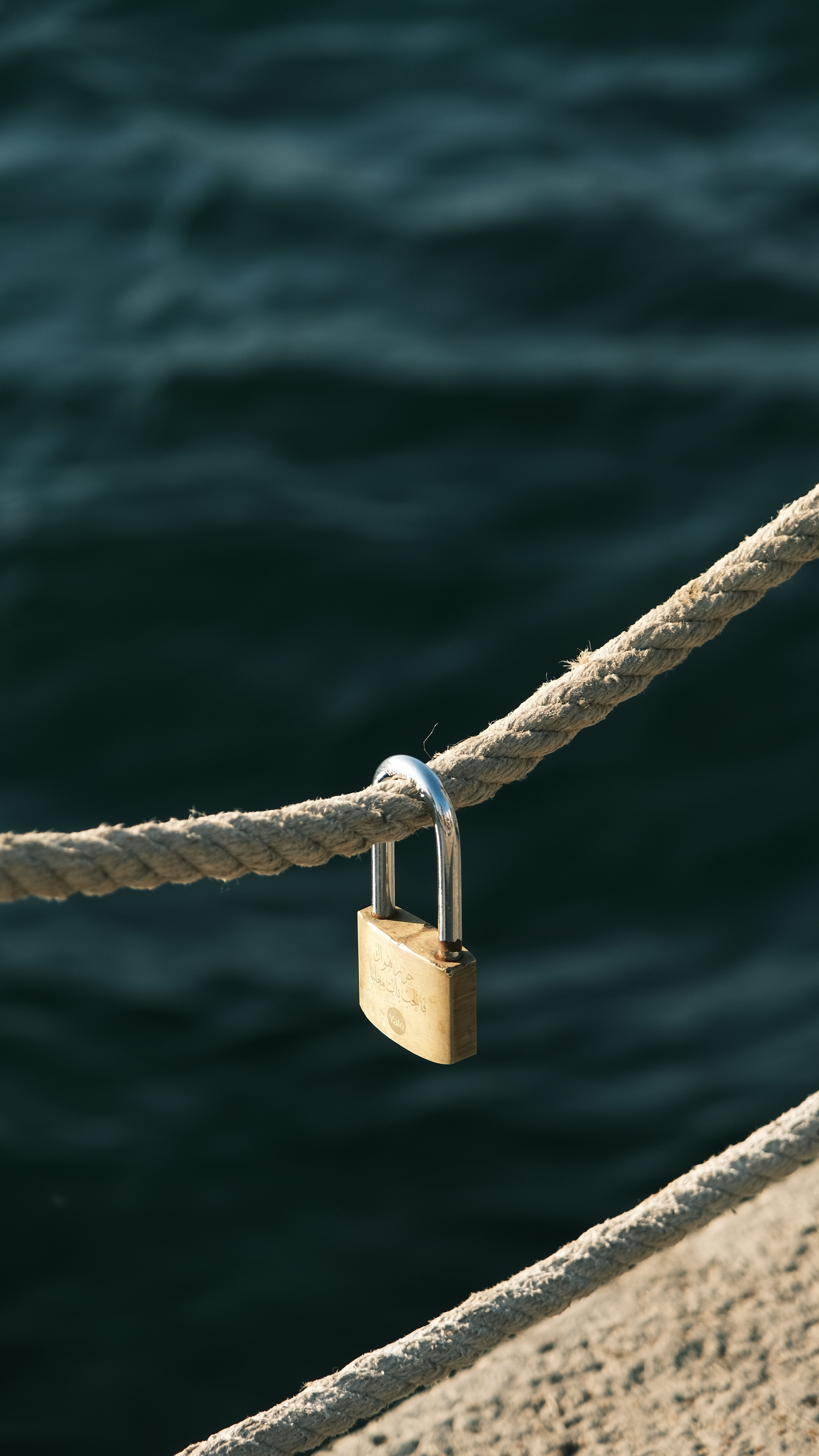 Close-up of a golden padlock secured on a rope against a blurred water background.