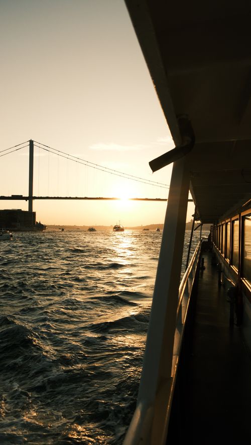 Free Serene sunset scene from a ferry with a bridge in the background, creating a peaceful seascape. Stock Photo