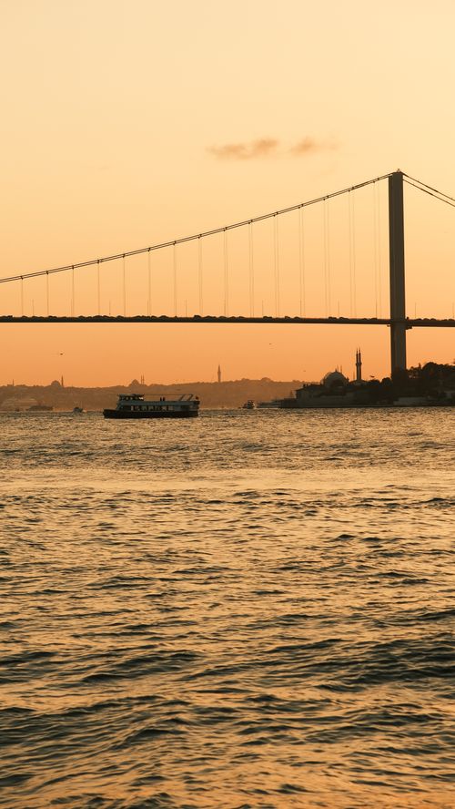 Free Serene sunset over Bosphorus Bridge in Istanbul, featuring calm waters and a ferry. Stock Photo