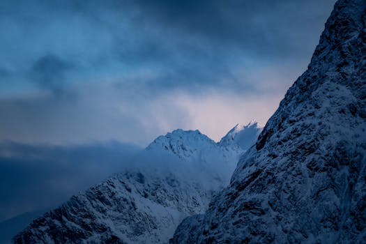 Captivating twilight view of snow-covered mountain peaks under a moody sky, exuding calmness and grandeur.