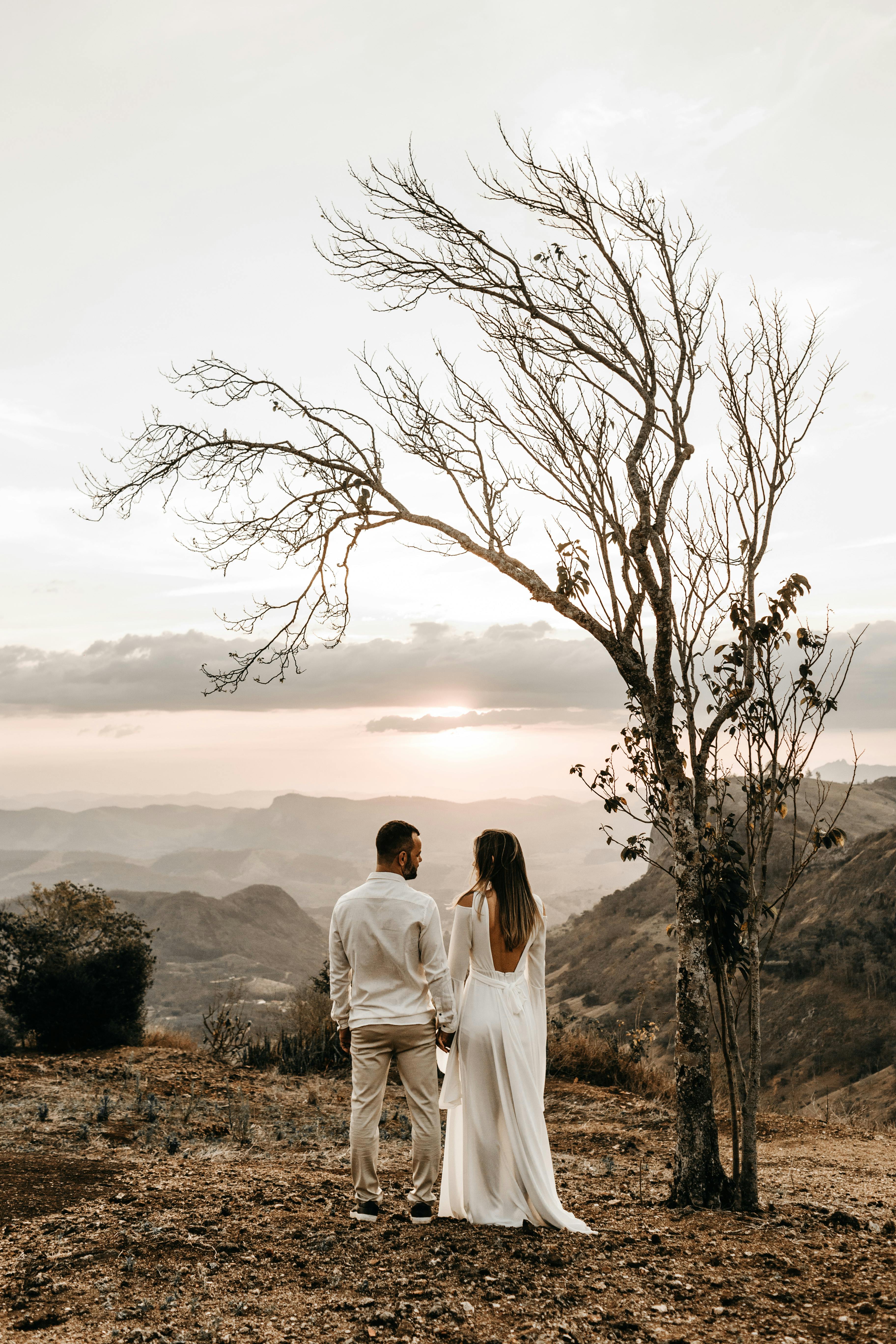 a couple in white dress standing in view of the mountain