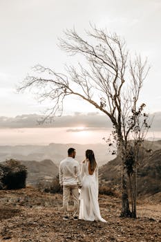 a couple in white dress standing in view of the mountain