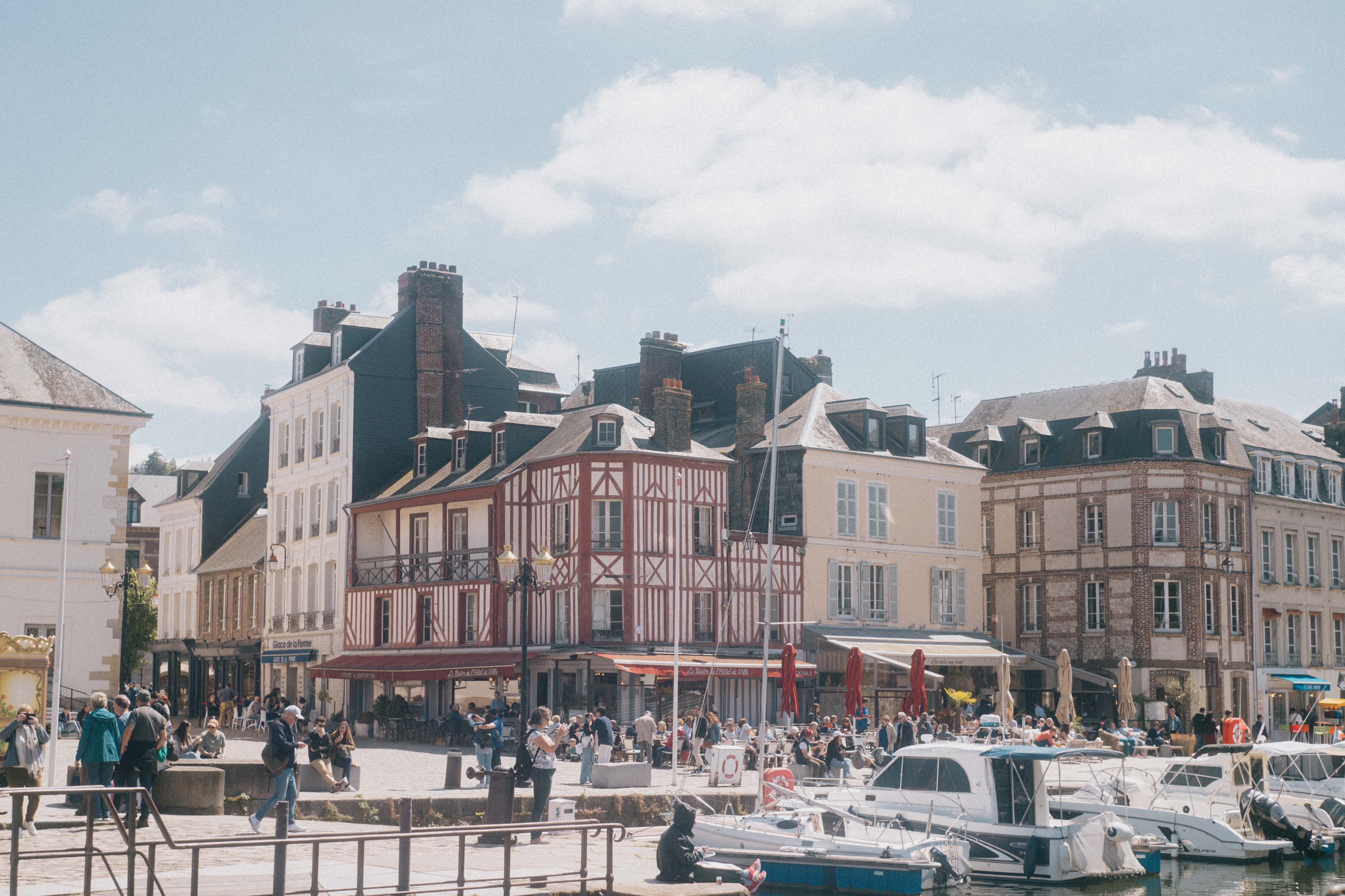 Sunny Honfleur waterfront square with busy outdoor café terraces, people and traditional French buildings