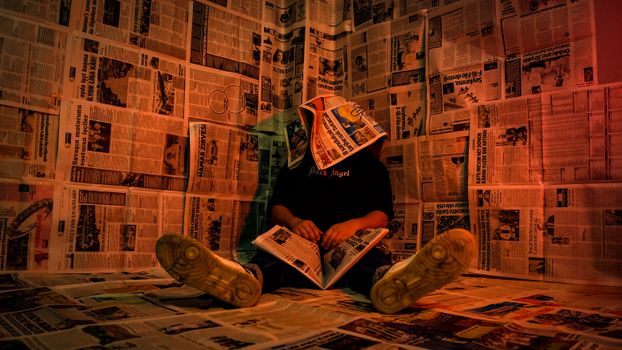 A person sits surrounded by newspapers, creating a unique, moody atmosphere.