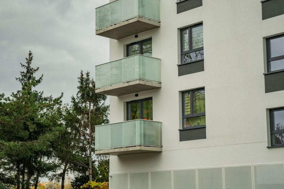 Contemporary apartment building with glass balconies and green surroundings.