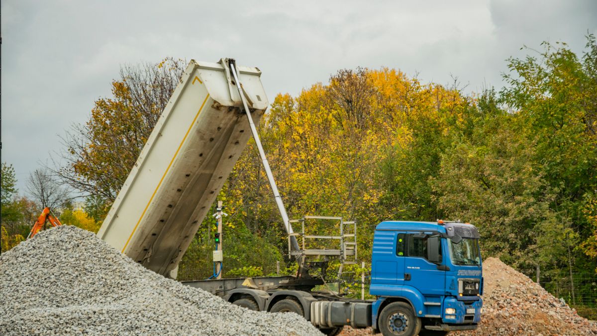 A dump truck tipping a load of gravel. Bulk yards sell by the cubic yard or the ton, so know both numbers before you call.