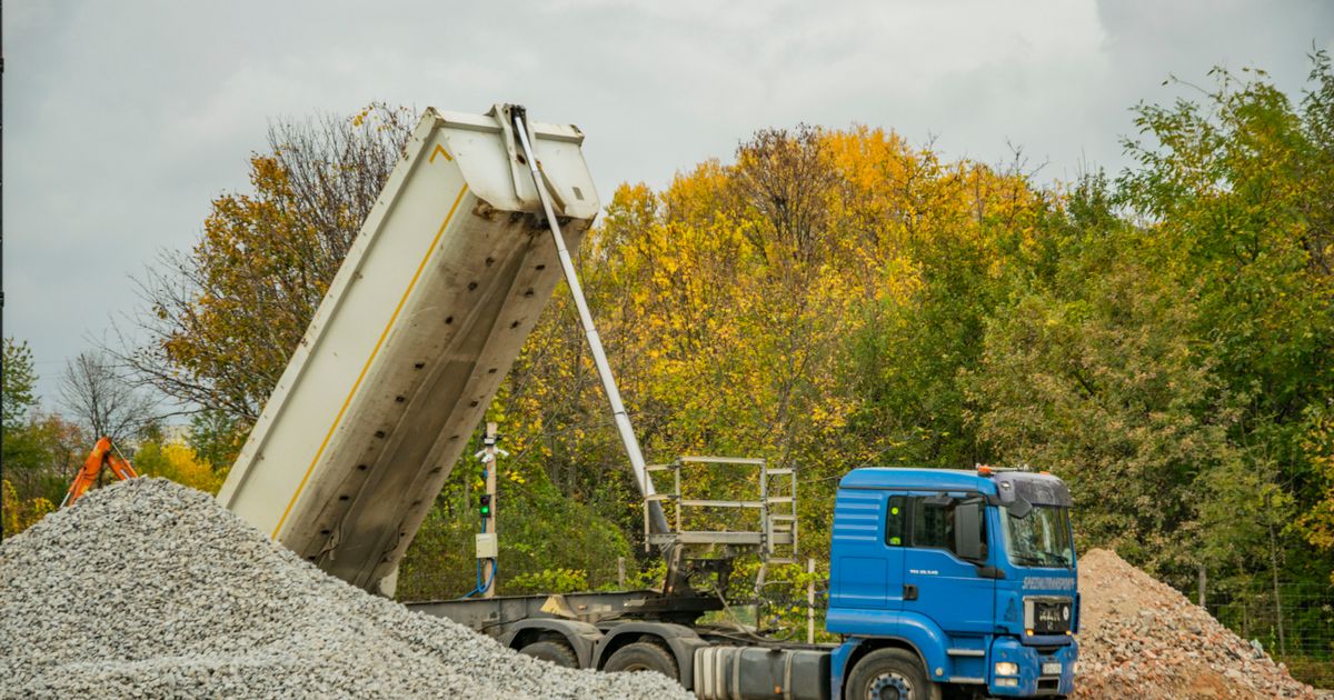 Blue dump truck unloading gravel at a construction site — the same material-displacement task a 500 kg mini dump truck on tracks handles on tight residential and commercial sites where larger machines cannot access