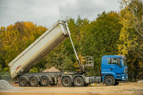 Free A blue dump truck unloading at a construction site surrounded by autumn foliage. Stock Photo