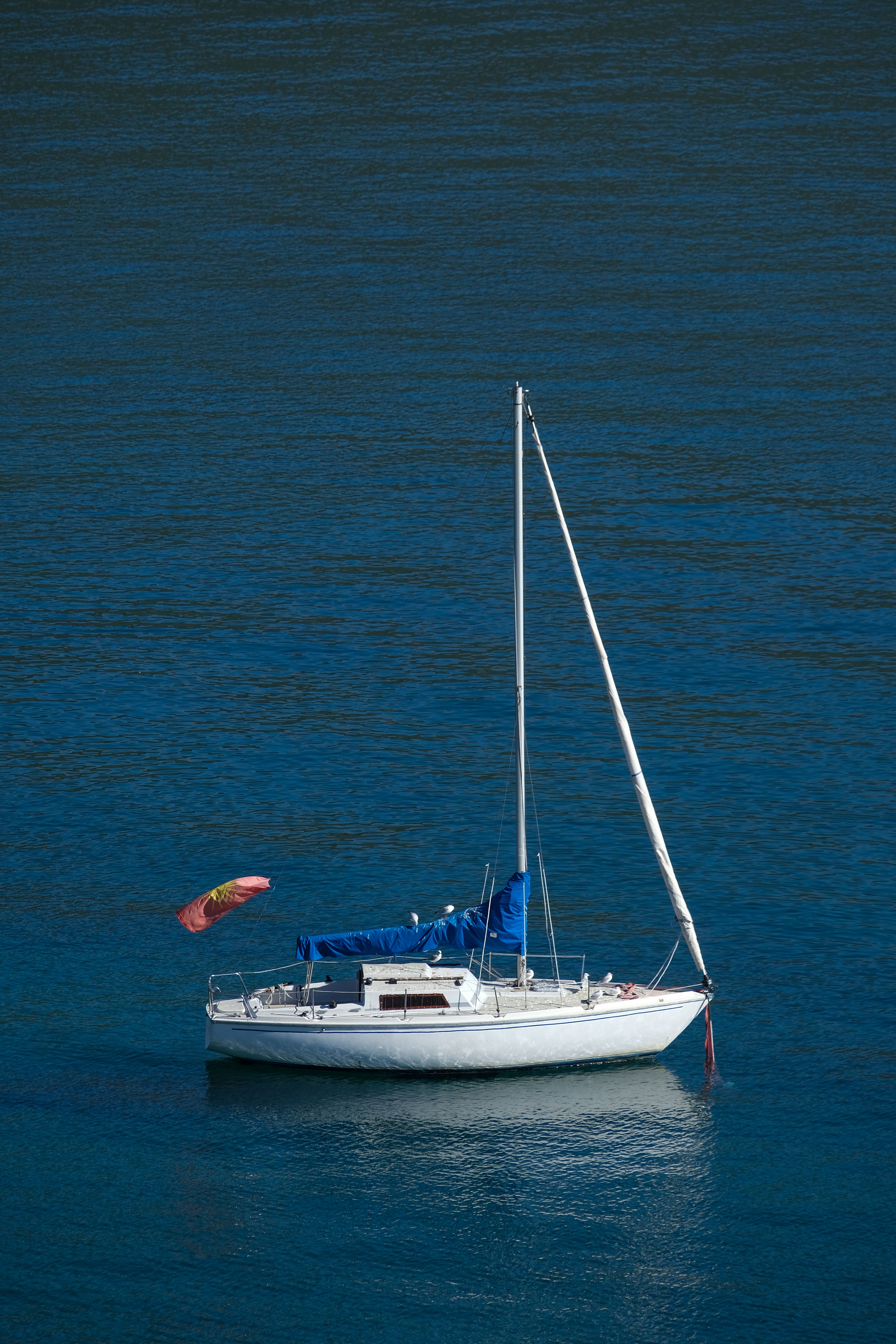 A lone sailboat floats peacefully on calm blue water under a clear sky.