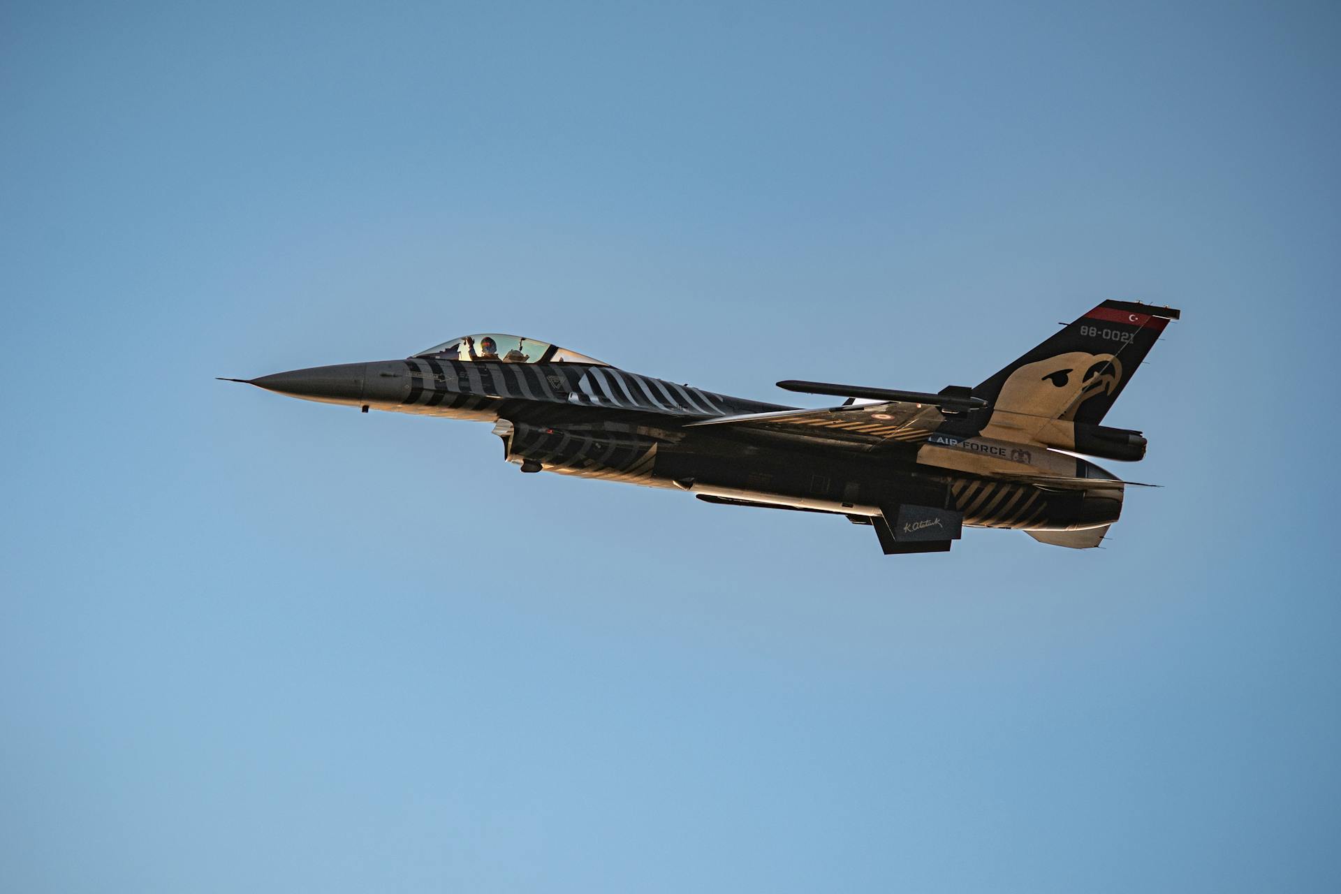 A dynamic image of an F-16 fighter jet soaring through a clear blue sky.