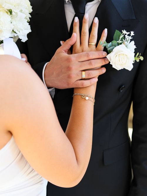 Free Close-up of a bride and groom holding hands, showcasing wedding rings and floral details. Stock Photo