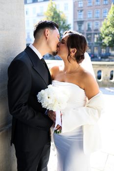 Bride and groom sharing a romantic kiss on their wedding day, outdoors.