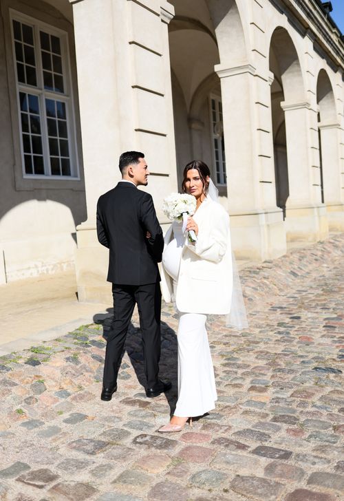 Free A stylish bride and groom walk together outside a historic building after their wedding ceremony. Stock Photo
