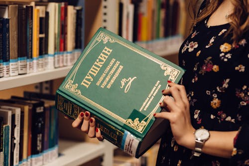 Woman Opening Book in Front of Bookshelf