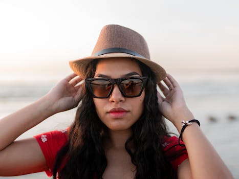 一位时尚女性戴着帽子和太阳镜，在海滩上欣赏日落
