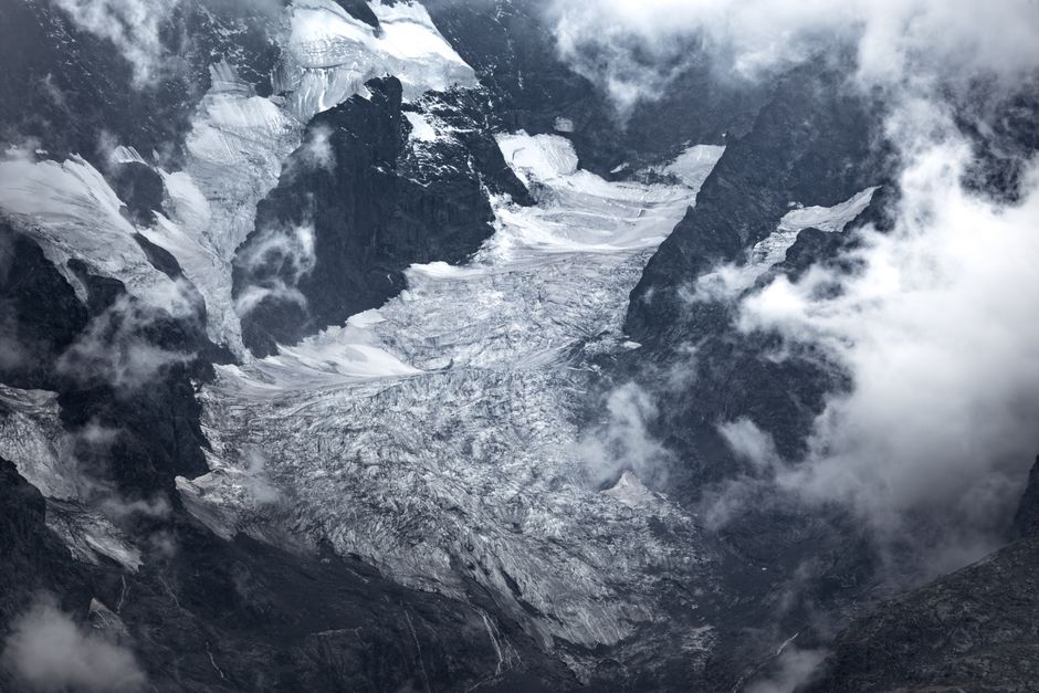 A striking aerial view of glaciers amidst the French Alps enveloped in clouds.