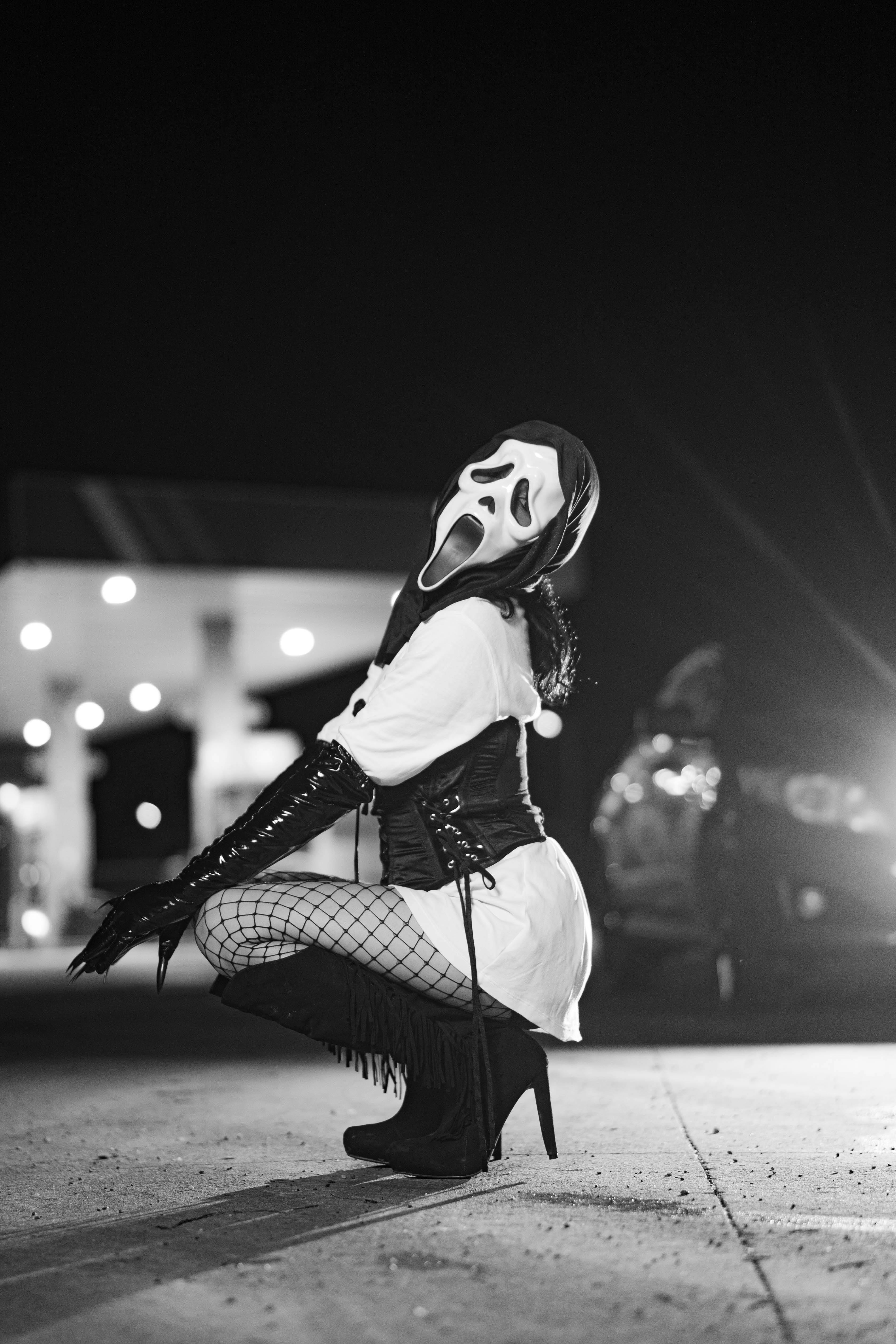 A figure in costume with a mask poses at a gas station at night, creating a haunting ambiance.