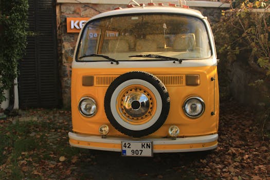 Front view of a yellow vintage campervan parked among autumn leaves.