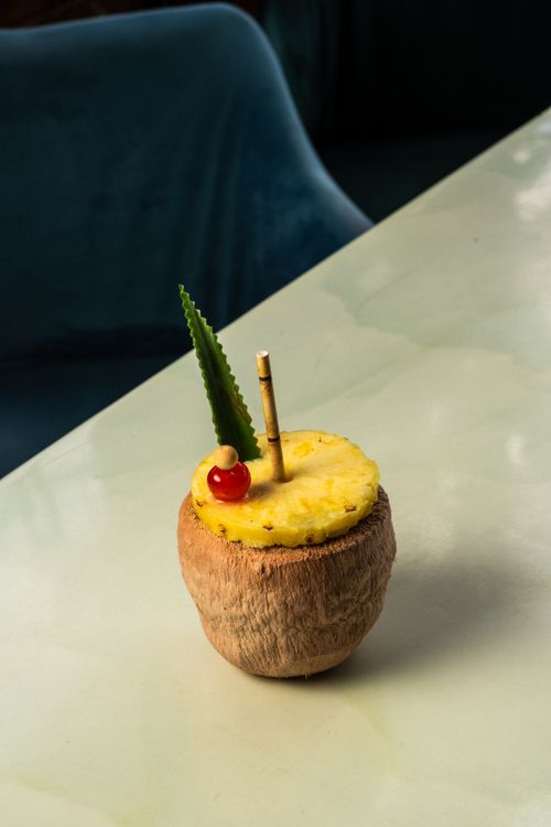 Free Refreshing tropical cocktail served in a coconut shell with pineapple and cherry garnish on a sleek table. Stock Photo