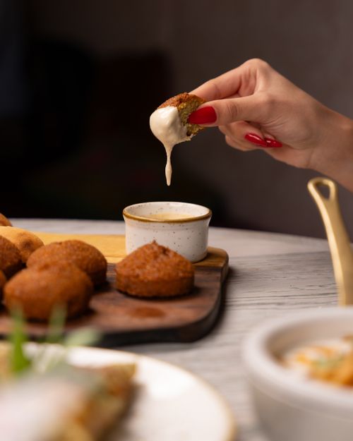 Free Hand dipping falafel into creamy sauce, showcasing a delicious Middle Eastern appetizer. Stock Photo