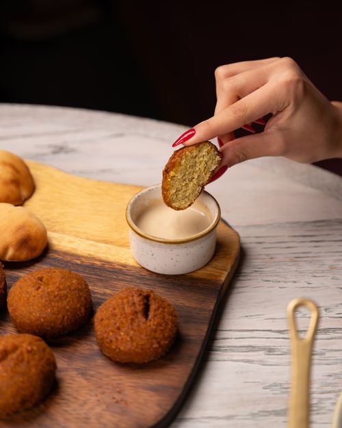 Free A person's hand dips falafel into tahini on a wooden platter, perfect for food concepts. Stock Photo