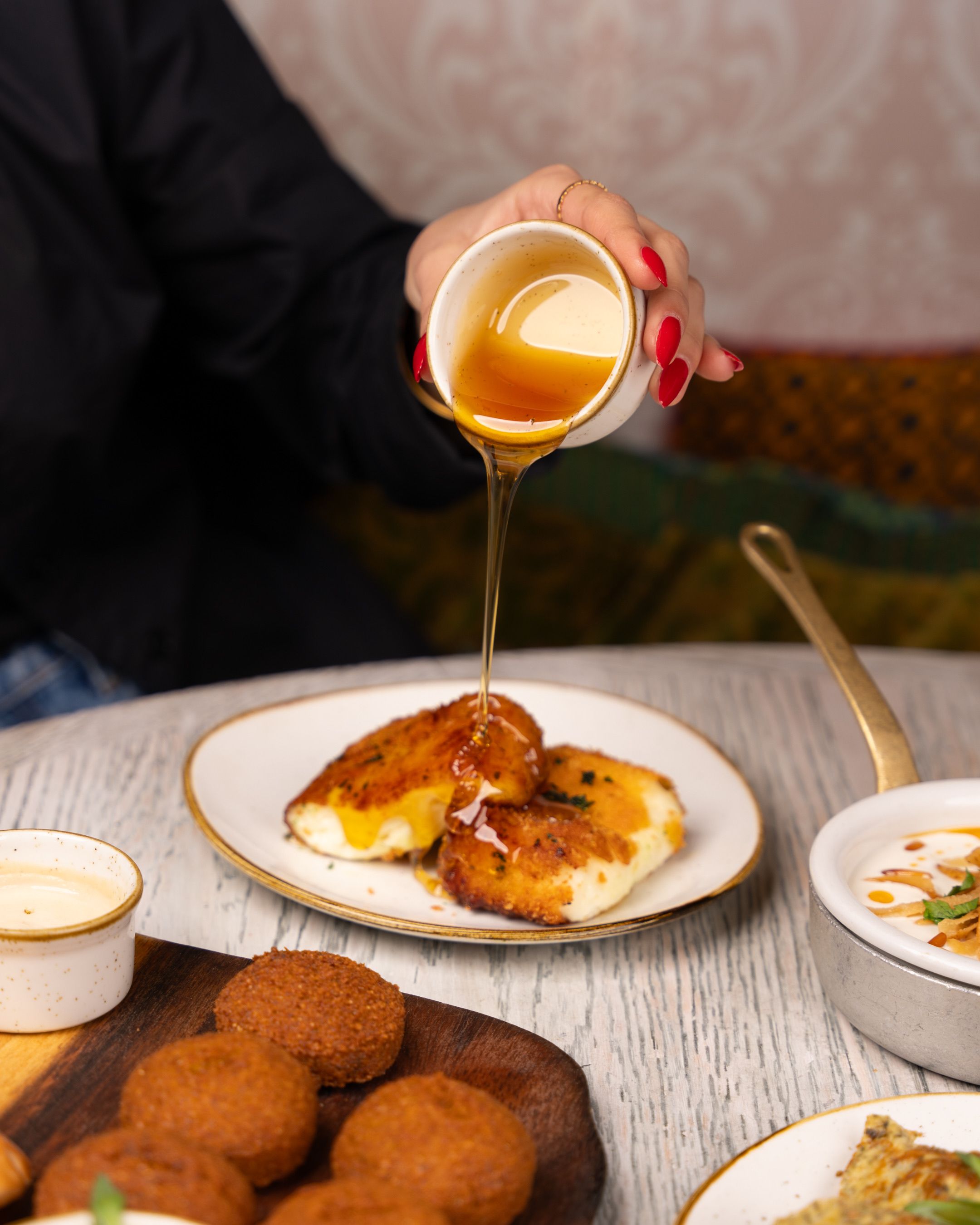 Close-up of hand pouring honey over fried cheese at a cafe table. Tasty appetizer.