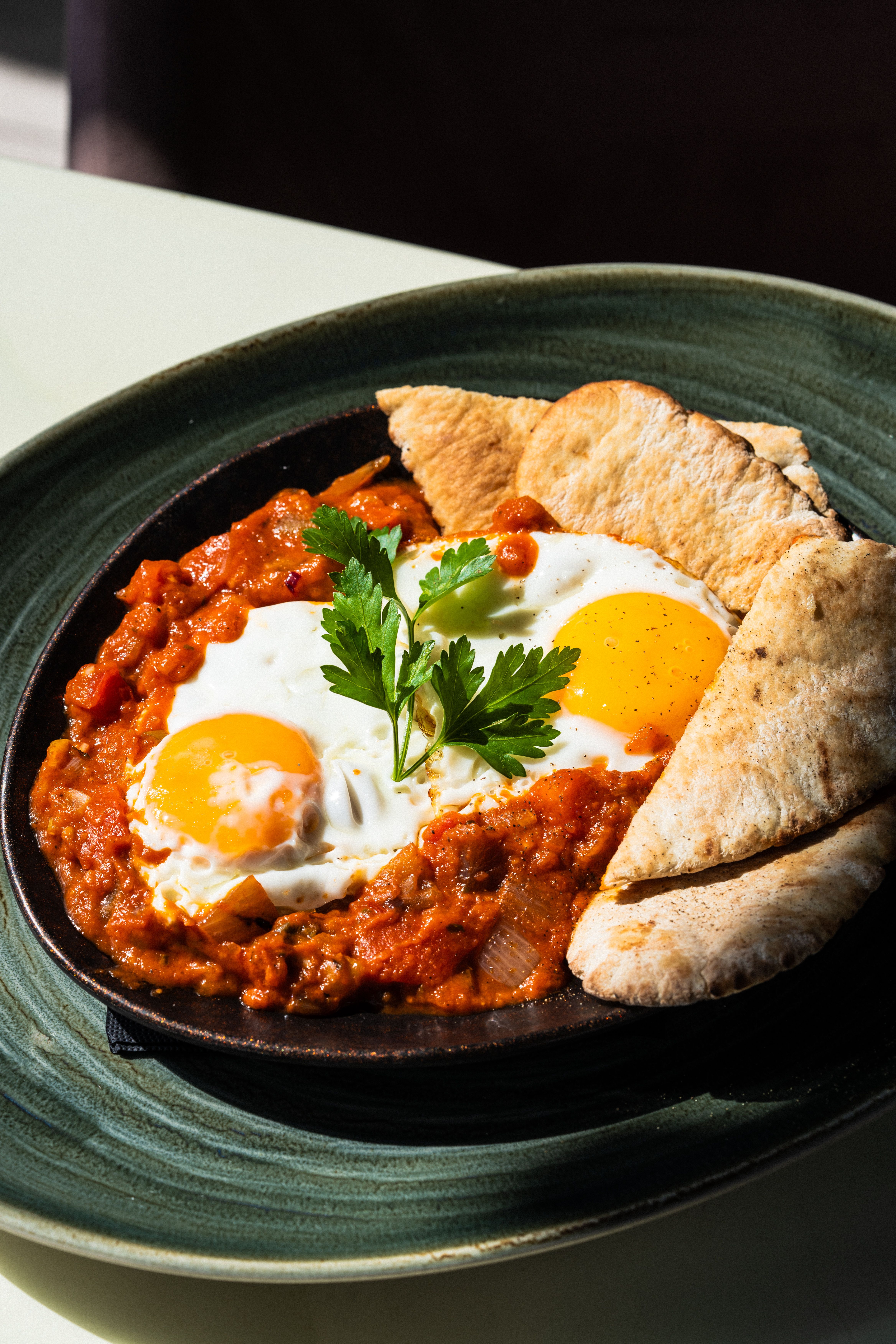 Tasty shakshouka with poached eggs served with pita bread on a green plate.
