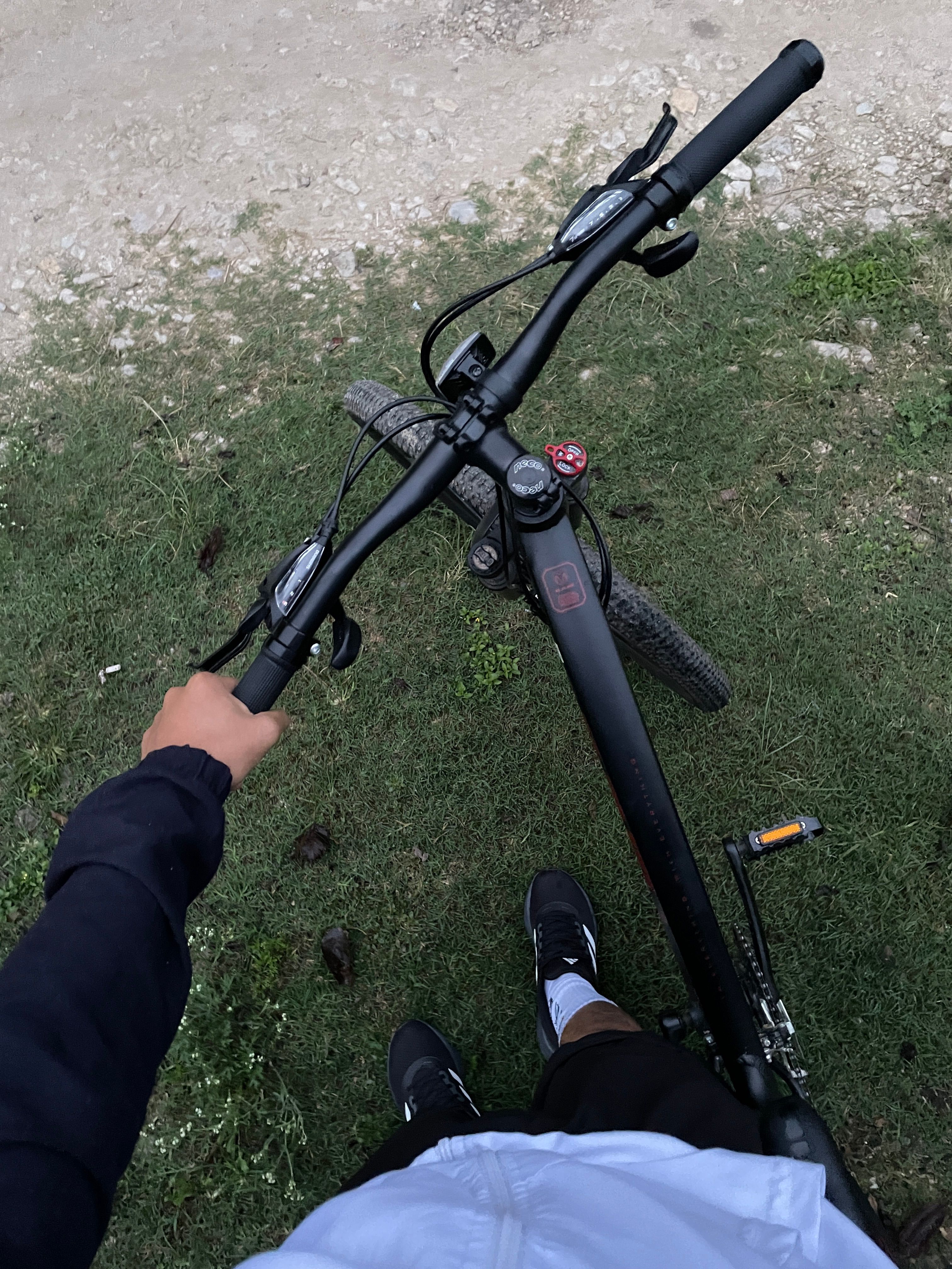 A first-person view of a cyclist gripping the handlebars of a mountain bike on a grassy trail.