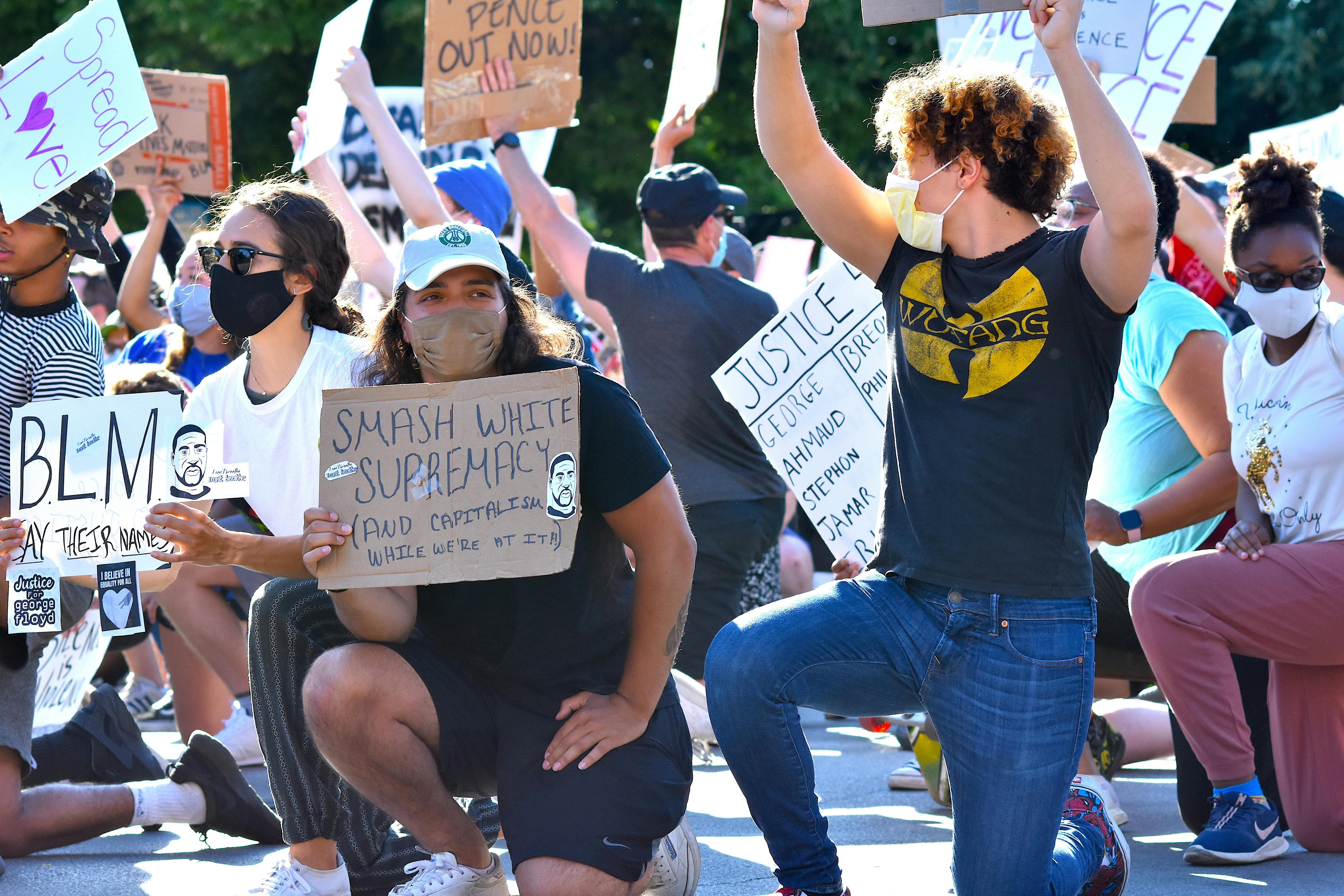 Protesters kneel with handwritten signs advocating for justice and equality at an outdoor demonstration.