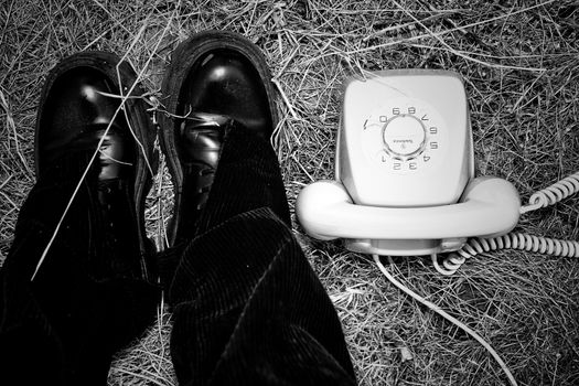 Black boots and vintage rotary phone on dry grass, an artistic scene in Las Palmas.