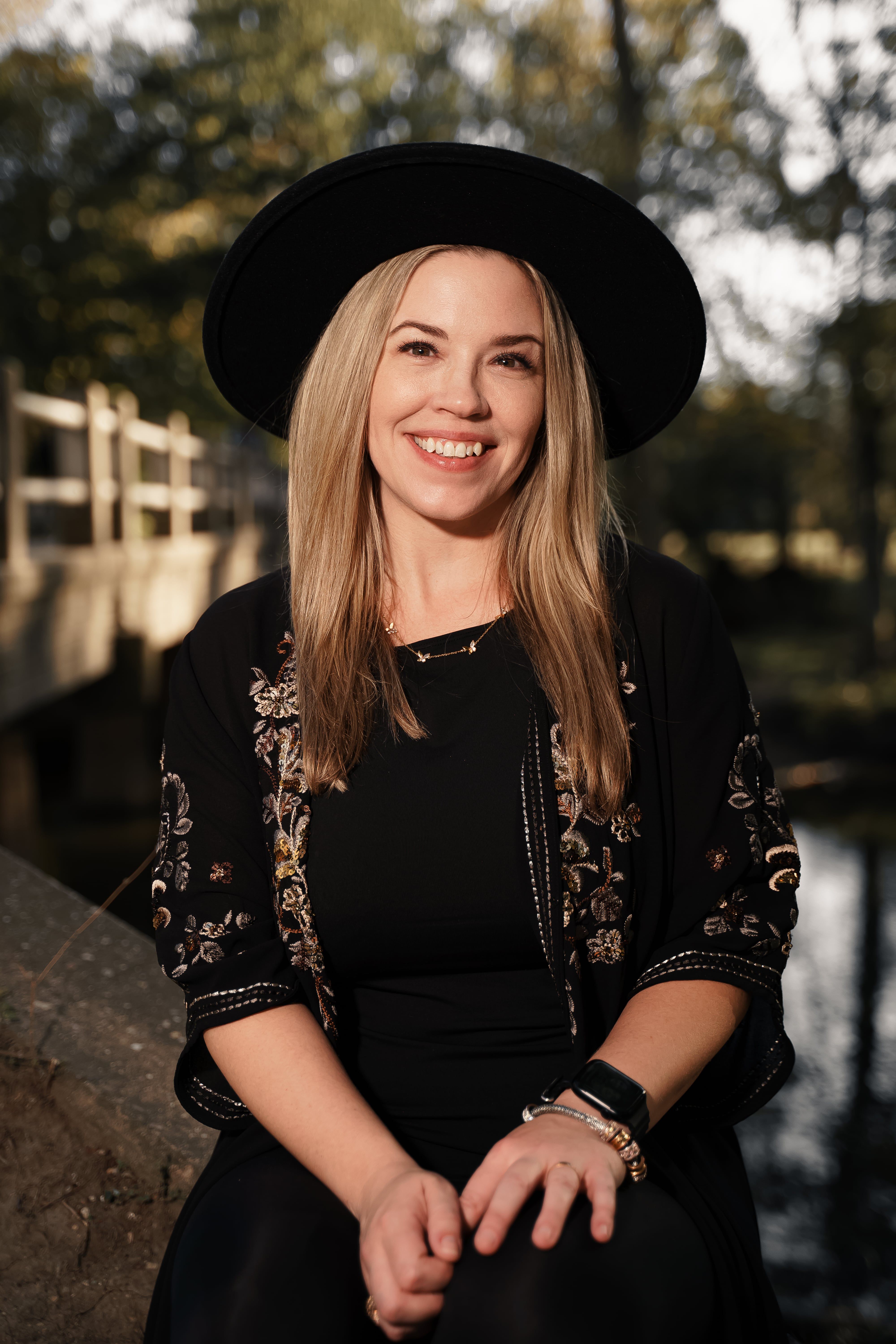 A joyful adult woman wearing a black hat, sitting outdoors with a charming smile.