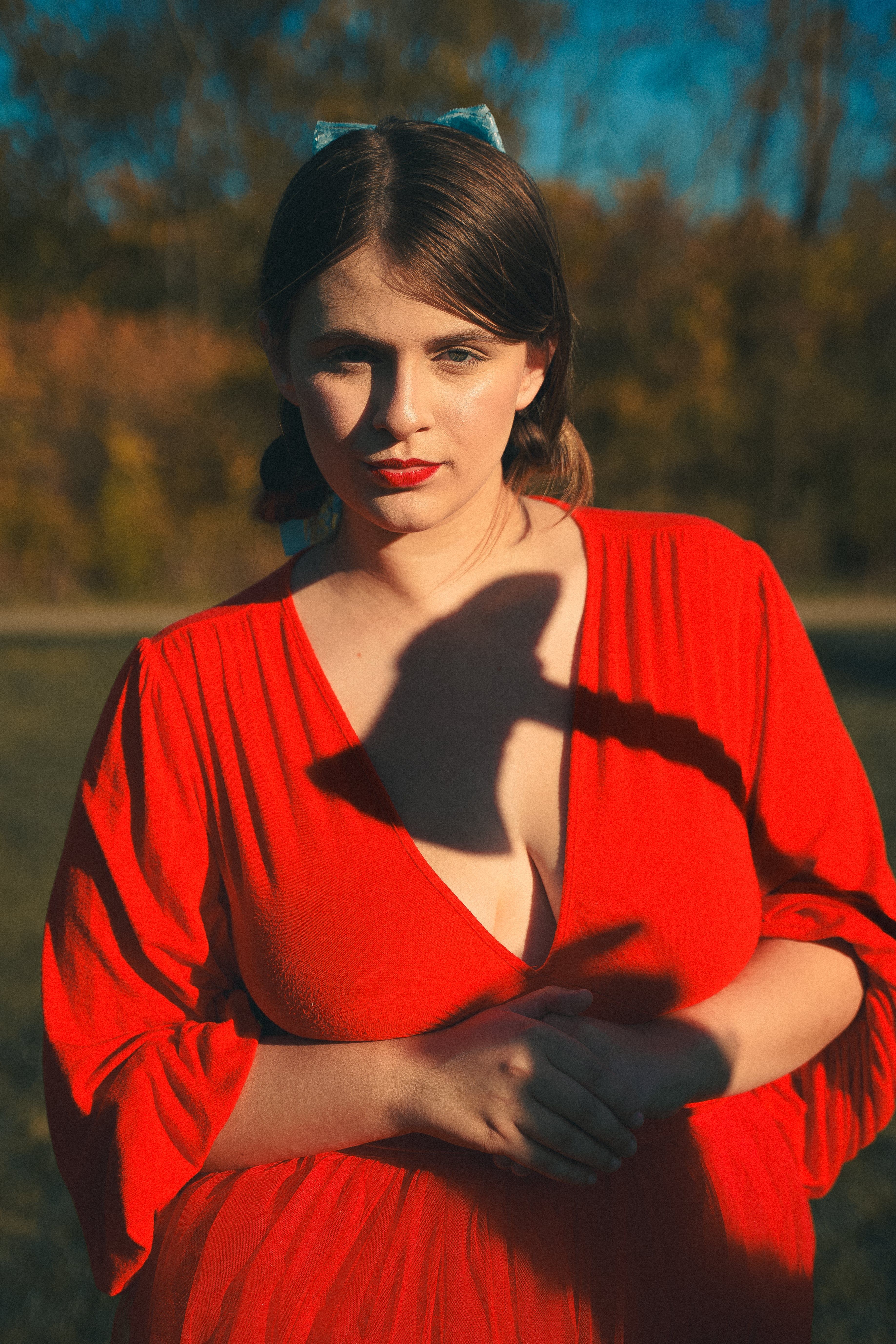 A woman in a vibrant red dress stands in an autumn setting with dramatic lighting.
