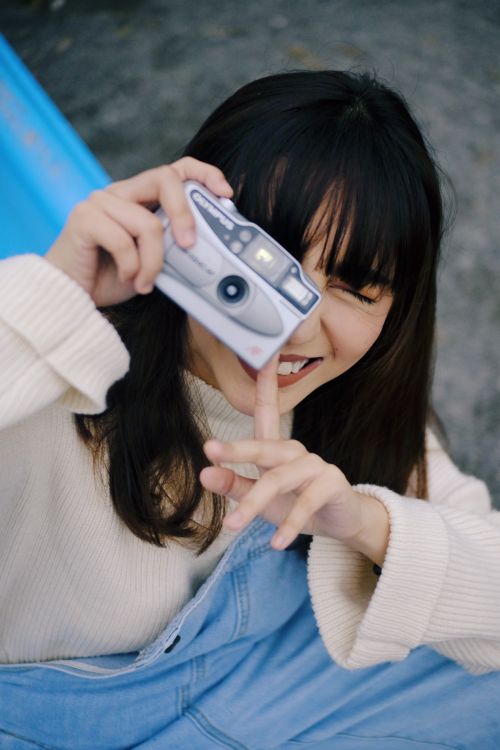 Free Young woman capturing joy with a camera during a sunny day. Perfect for lifestyle themes. Stock Photo