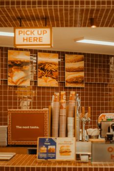 A fast food restaurant counter with menu displays and a 'Pick Up Here' sign.
