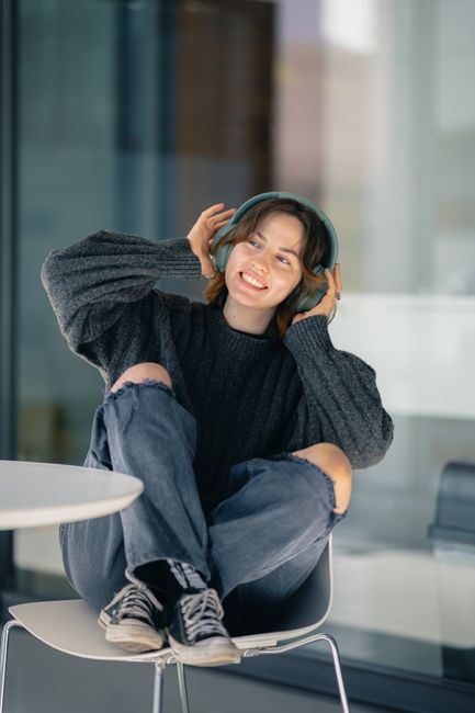 Smiling young woman in casual attire listening to music with headphones indoors.