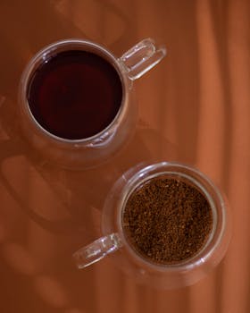 Top view of ground coffee and brewed drink in glass cups on an orange surface.
