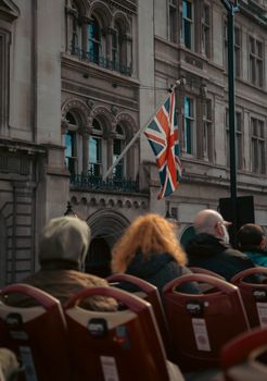 Group of tourists watching Union Jack flag outside a historic building in London.