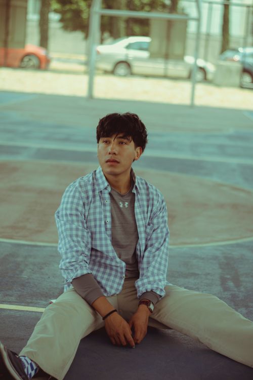 Free Casually dressed young man sitting on an outdoor basketball court in a relaxed pose. Stock Photo