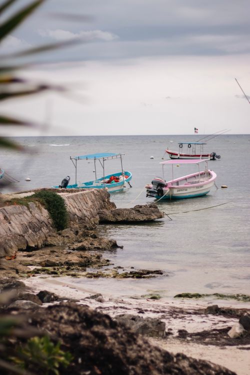 Free Serene ocean scenery with boats anchored near a rocky pier on a cloudy day. Stock Photo